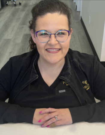 a person sitting at a table with a laptop and smiling at the camera